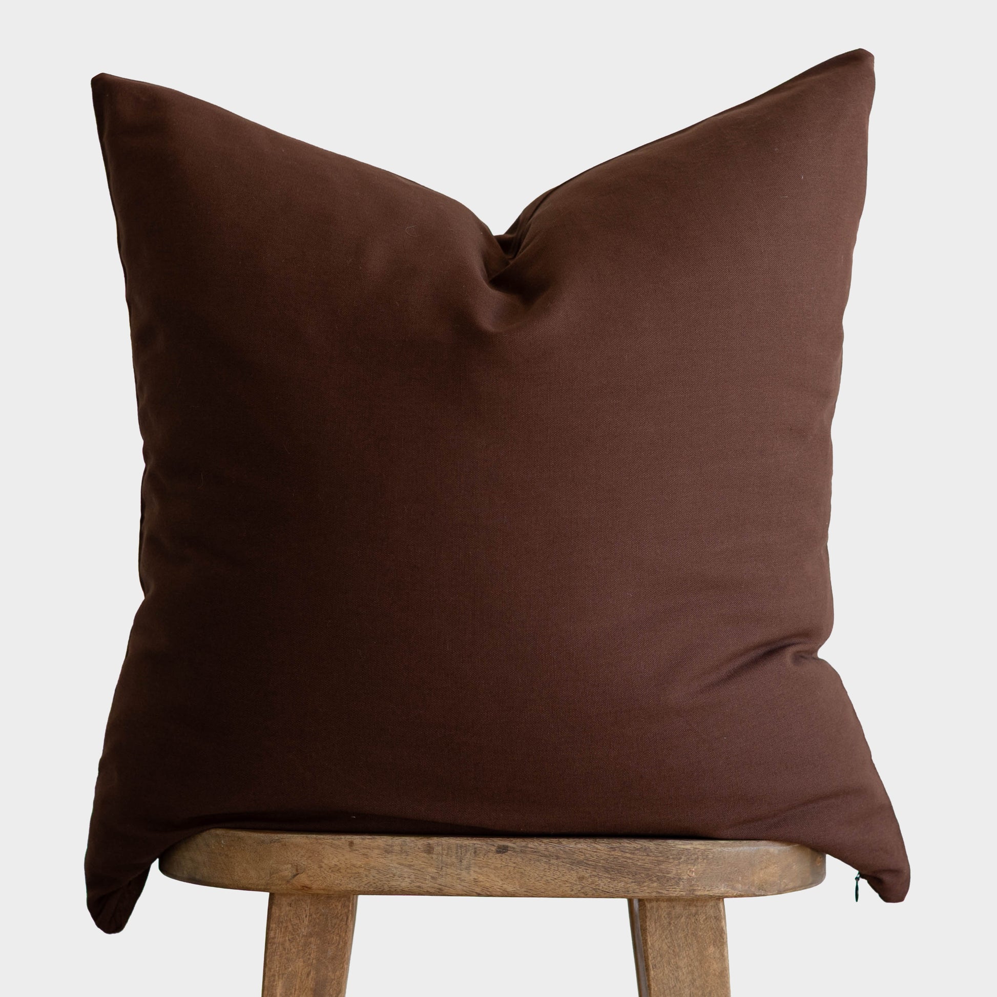 Brown linen pillow cover draped over wooden chair back against white background.