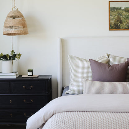 Tan lumbar pillow with subtle pattern displayed on bed with gingham and striped pillows.