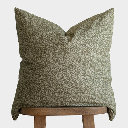 Green cushion with leafy botanical print pattern displayed on wooden chair.