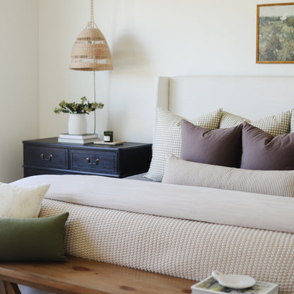 Tan lumbar pillow displayed on a bed with checkered and striped bedding, styled in a bedroom setting.