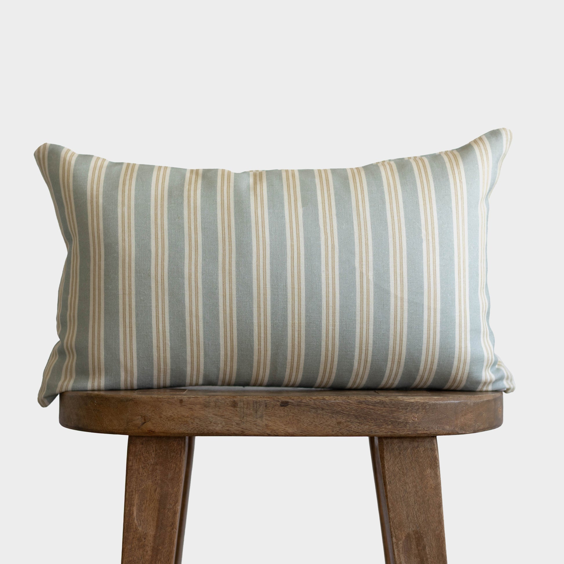 Rectangular pillow with vertical stripes in gray, beige, and cream on wooden stool.