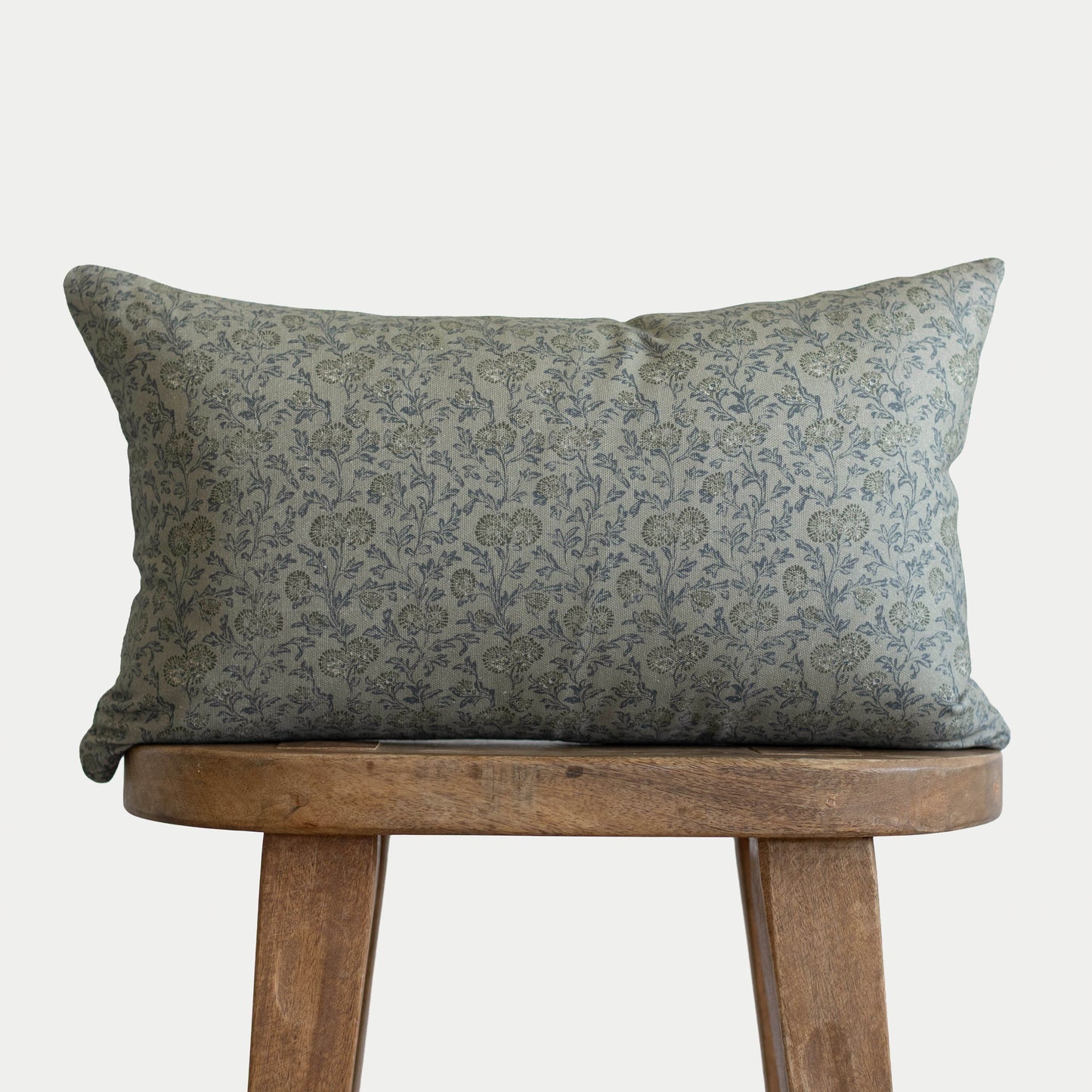 Green damask patterned lumbar pillow displayed on wooden stool.