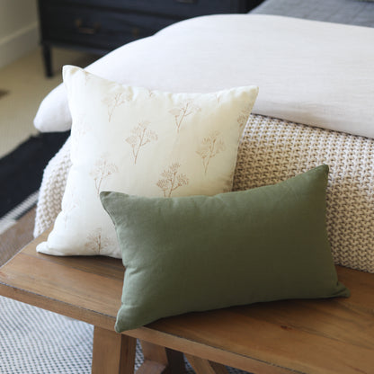 Cream pillow with tan botanical pattern and sage green rectangular pillow on wooden table.