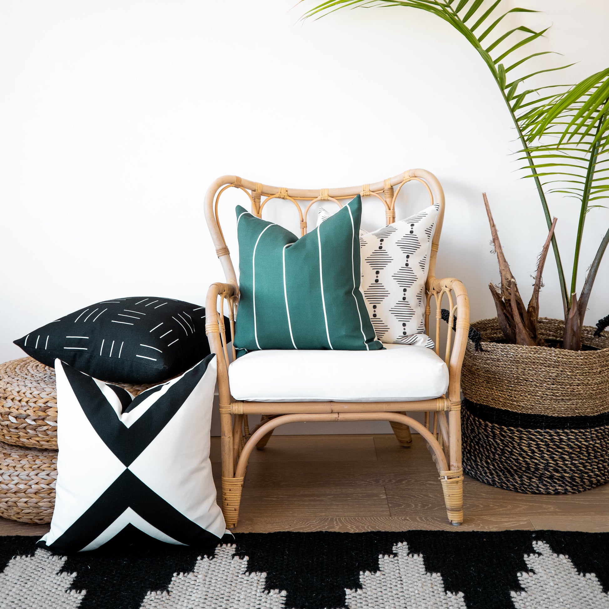 Four outdoor pillow covers in teal striped, cream geometric, black striped, and black-white geometric patterns displayed on r