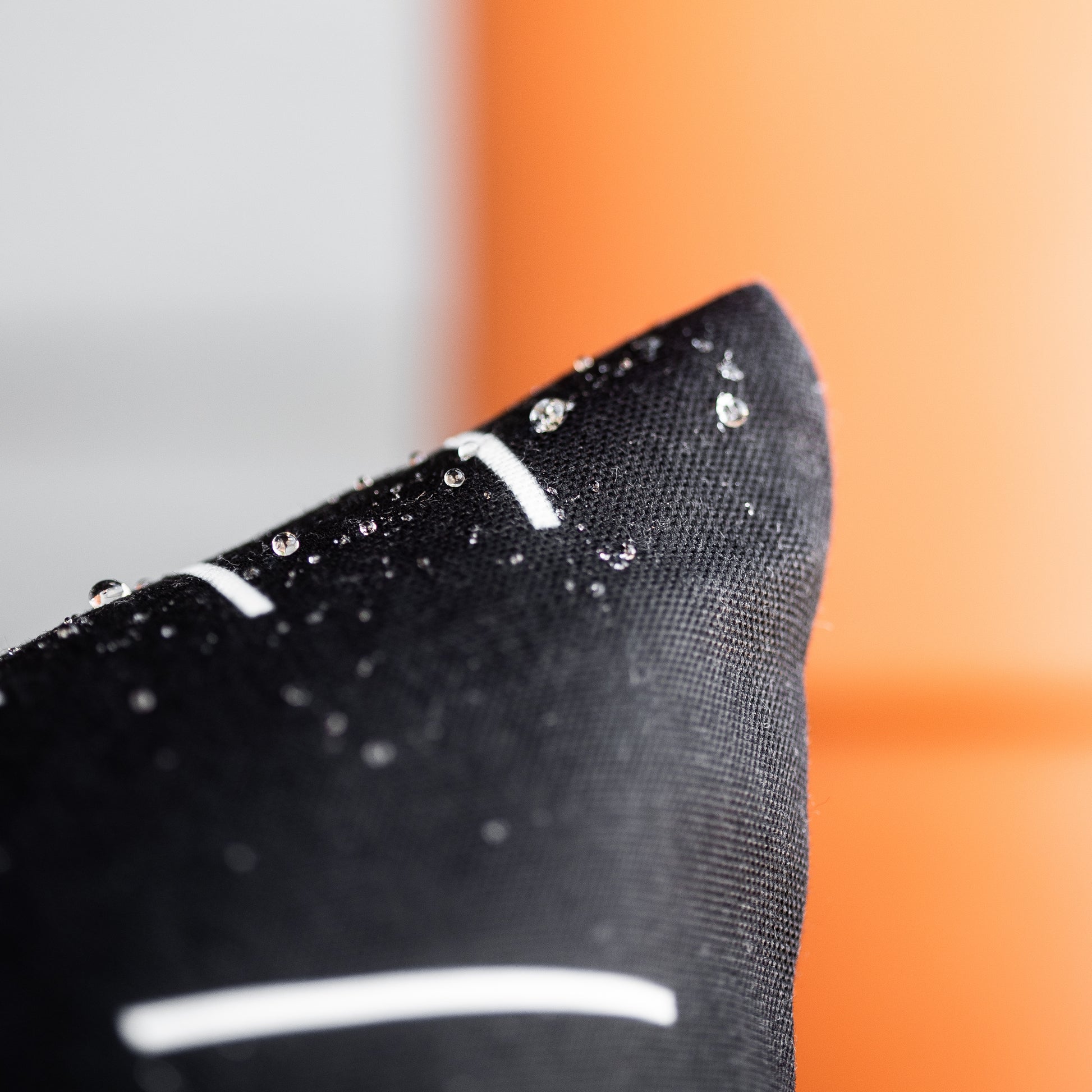 Black outdoor pillow cover with water beads on textured fabric surface.