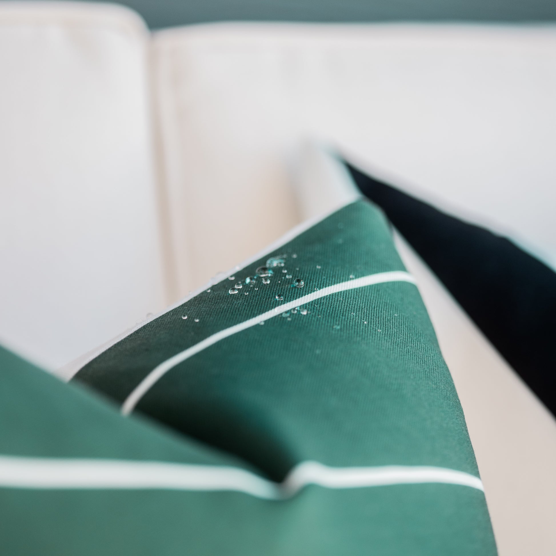 Teal and cream outdoor pillow covers stacked together showing water-beading fabric texture with white piping details.
