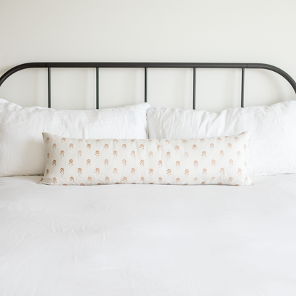 Long lumbar pillow with peach floral pattern on white background, displayed on bed with white pillows and black metal headboa