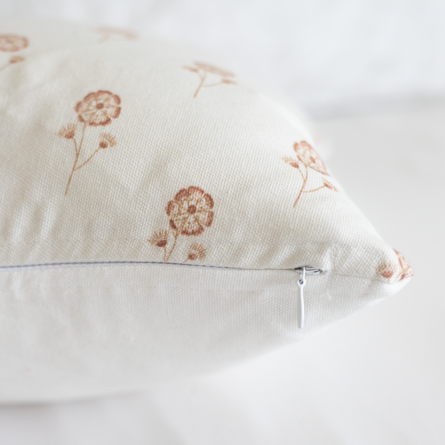 Cream-colored pillow with rust dandelion print and hidden zipper closure.