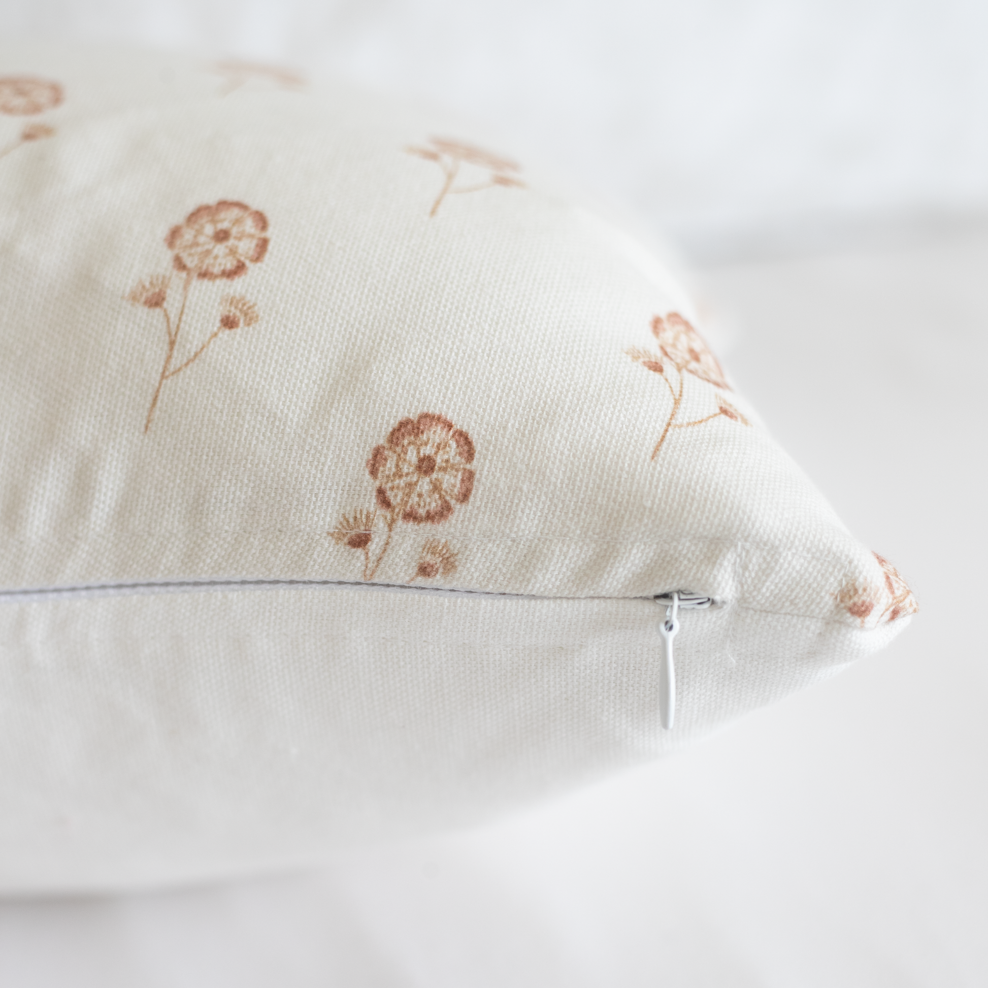 Cream-colored pillow with rust dandelion print and hidden zipper closure.