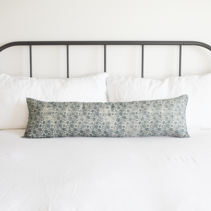 Blue and cream floral patterned lumbar pillow on a bed with white bedding and metal headboard.