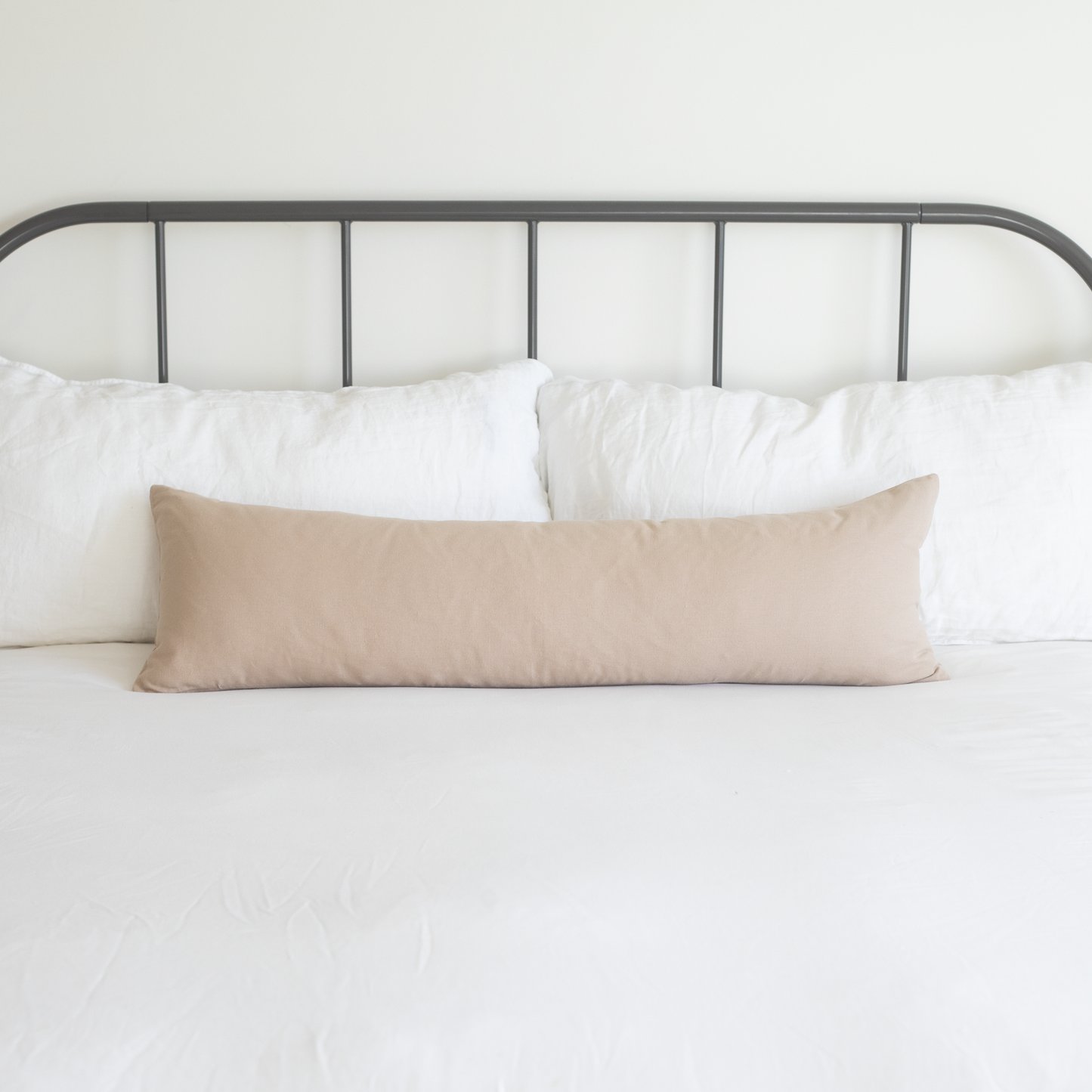Tan lumbar pillow displayed on a bed with white pillows and metal headboard.