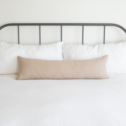 Tan lumbar pillow displayed on a bed with white pillows and metal headboard.