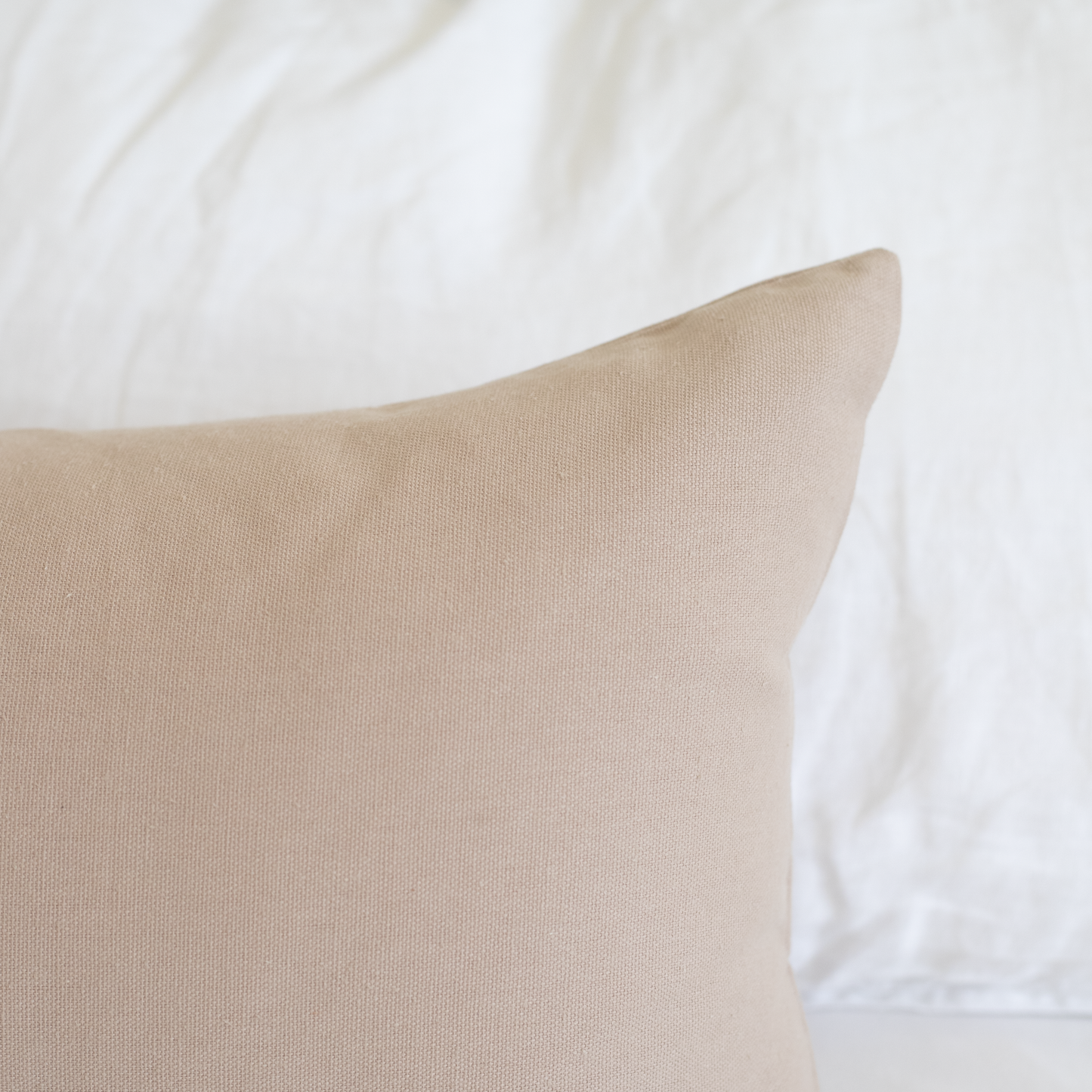 Tan rectangular pillow with textured weave fabric displayed against white bedding.
