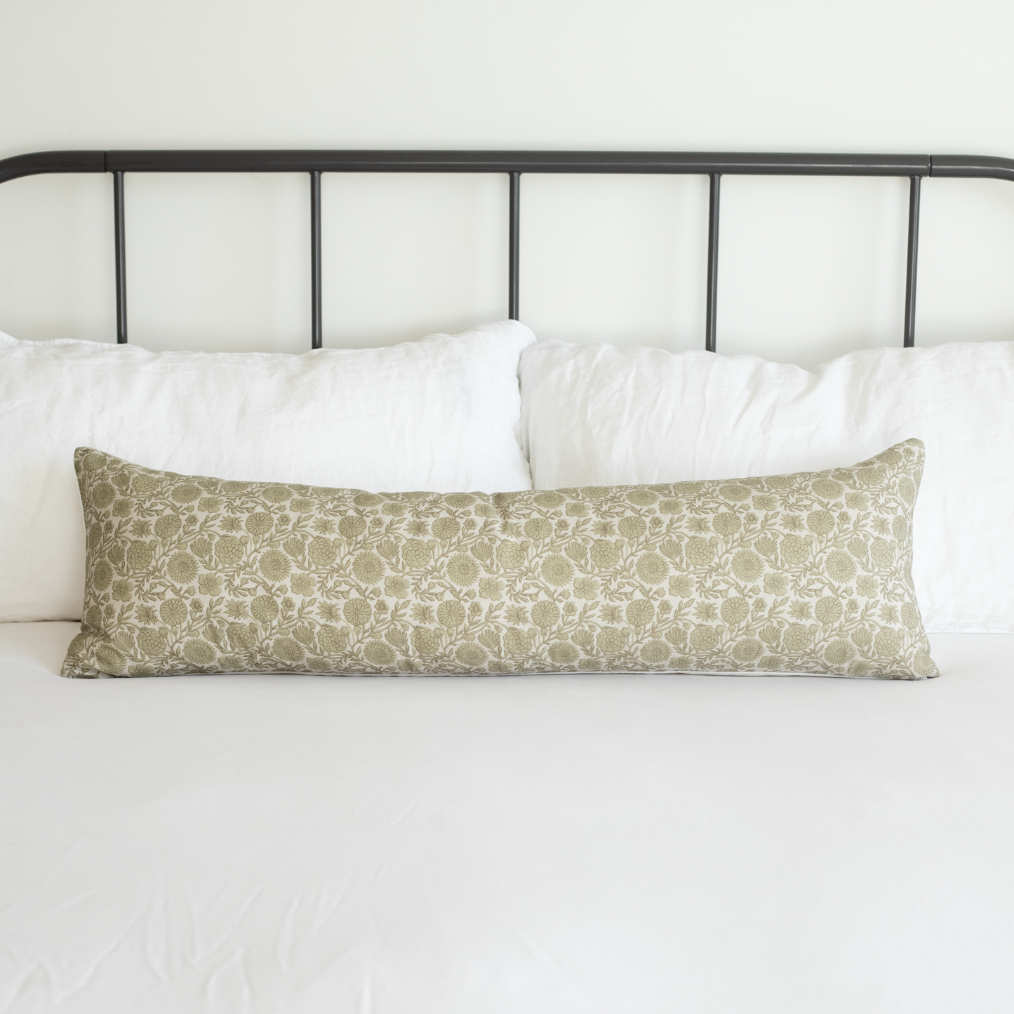 Long rectangular lumbar pillow with green and cream floral botanical print, displayed on bed with white pillows and black met