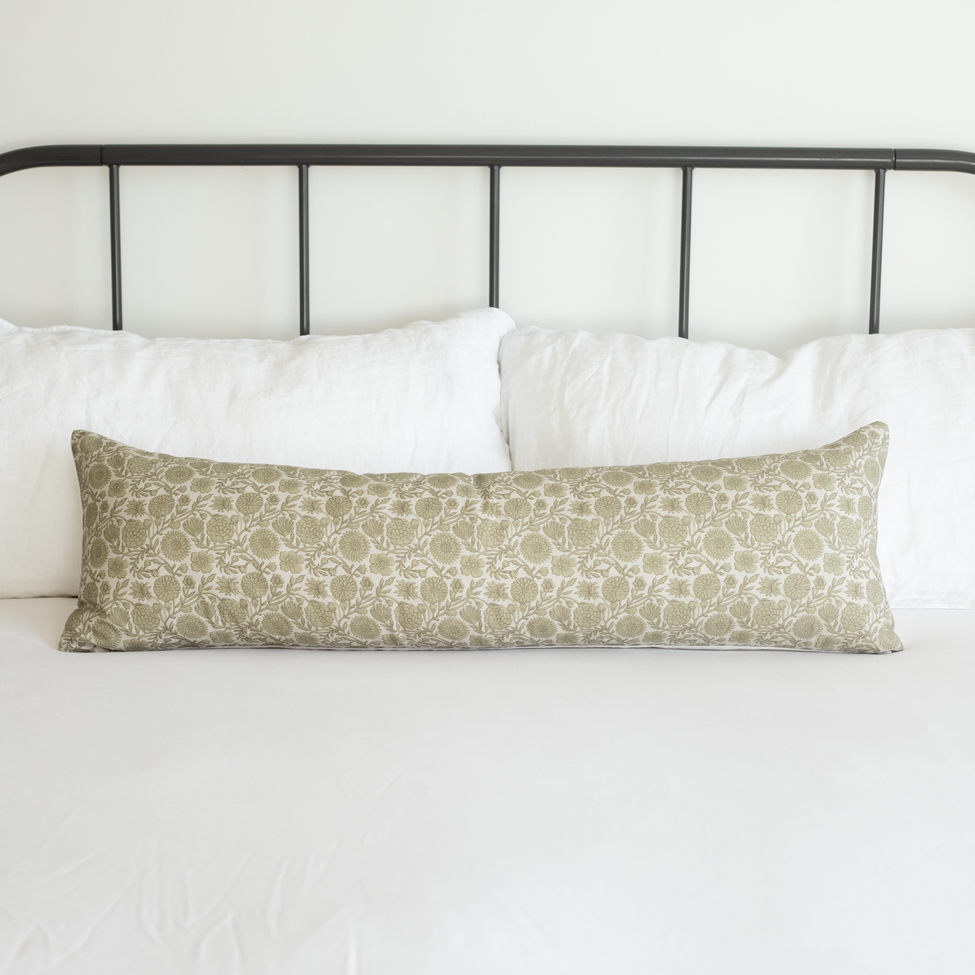 Long rectangular lumbar pillow with green and cream floral botanical print, displayed on bed with white pillows and black met