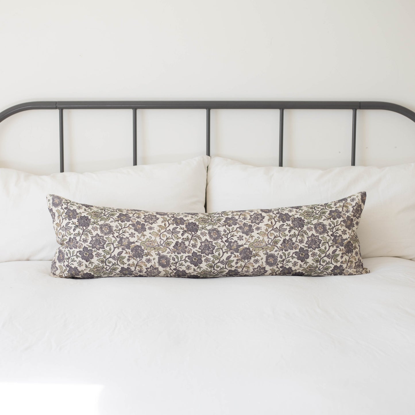 Gray and cream floral lumbar pillow on a bed with metal headboard and white bedding.
