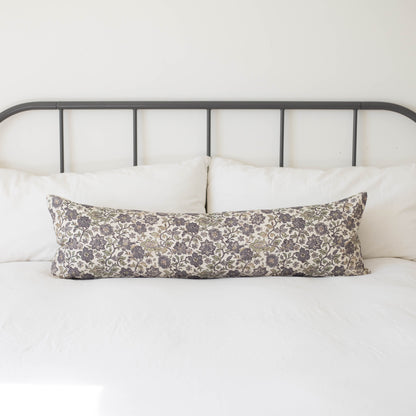Gray and cream floral lumbar pillow on a bed with metal headboard and white bedding.