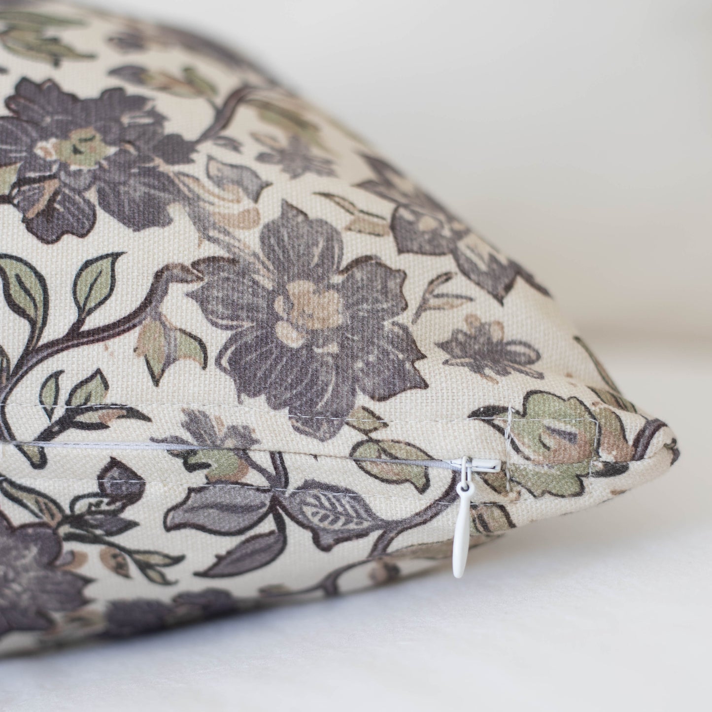 Cream pillow with dark gray and sage floral pattern, zipper closure visible on side.