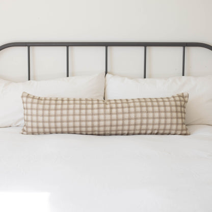 Beige and cream gingham patterned cotton lumbar pillow on white bedding with metal headboard.