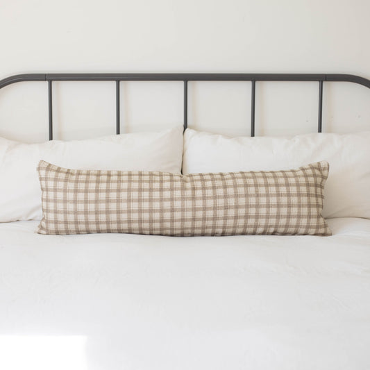 Beige and cream gingham patterned cotton lumbar pillow on white bedding with metal headboard.