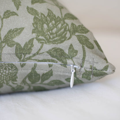 Cream pillow with green botanical leaf and flower print, white zipper closure visible on side.