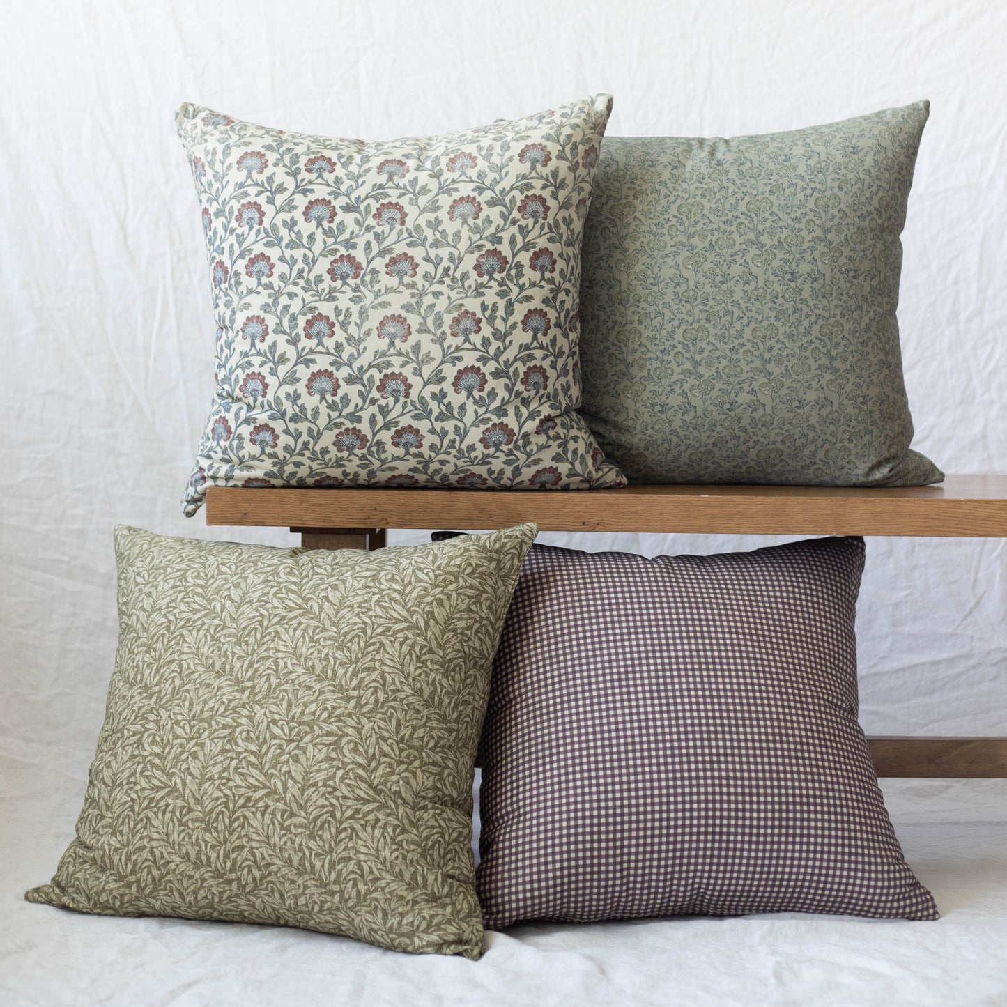 Four decorative pillows in varying floral and geometric patterns in green, cream, and burgundy tones displayed on a wooden sh
