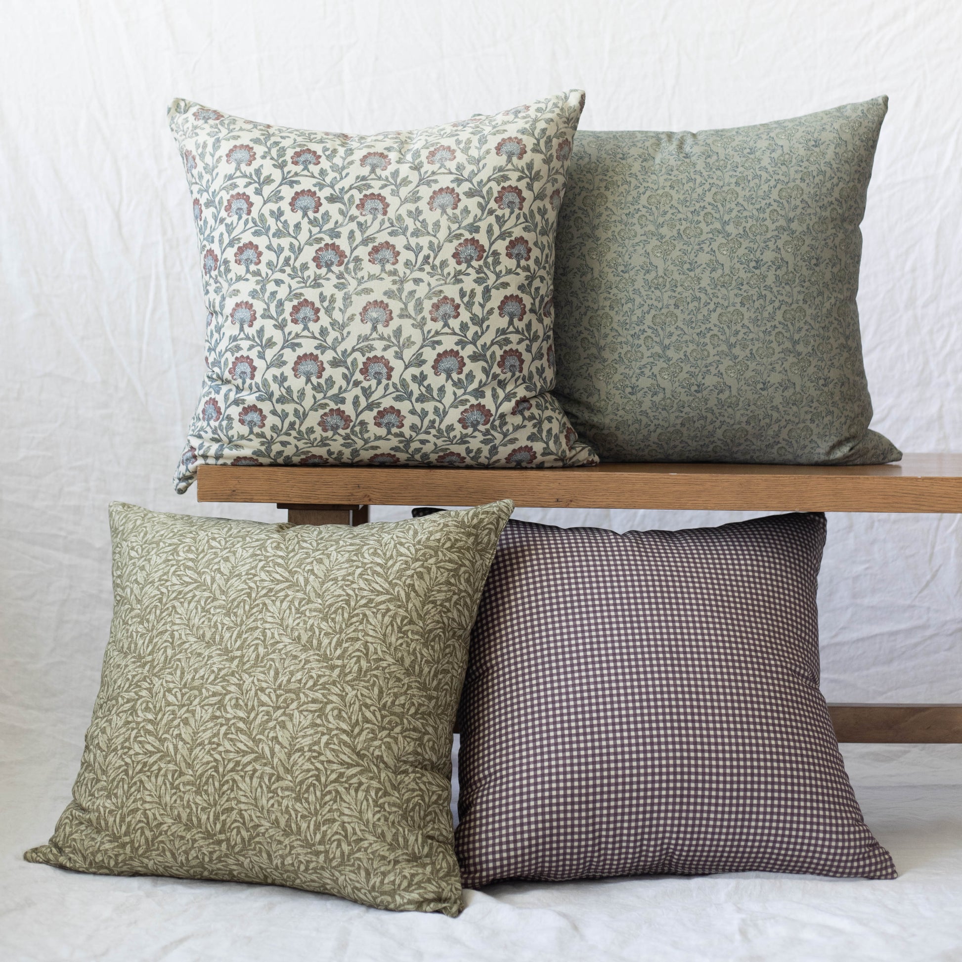 Four decorative pillows in varying floral and geometric patterns in green, cream, and burgundy tones displayed on a wooden sh