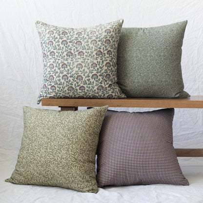 Four decorative pillows in varying floral and geometric patterns in green, cream, and burgundy tones displayed on a wooden sh
