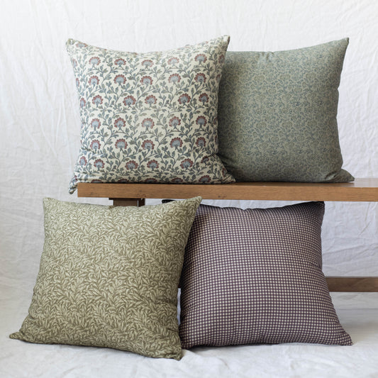 Four decorative pillows in varying floral and geometric patterns in green, cream, and burgundy tones displayed on a wooden sh