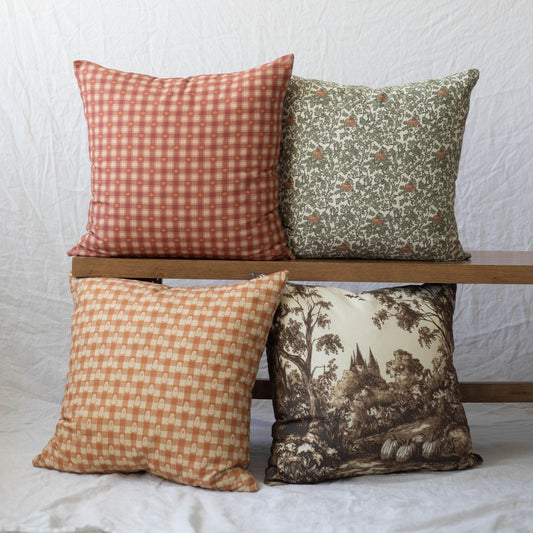 Four decorative pillows in red gingham, green floral, orange geometric, and brown landscape prints.