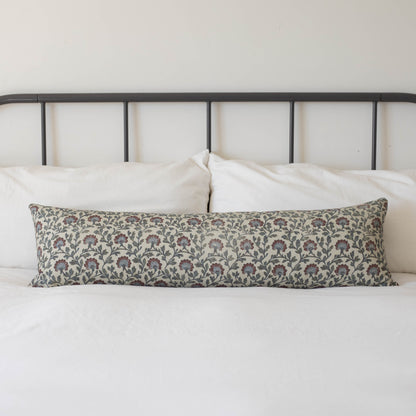 Multicolor floral patterned lumbar pillow with burgundy and blue flowers on cream background, displayed on bed with metal hea