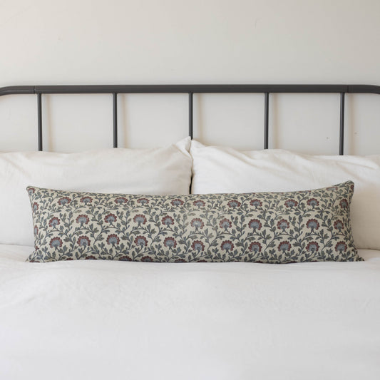 Multicolor floral patterned lumbar pillow with burgundy and blue flowers on cream background, displayed on bed with metal hea