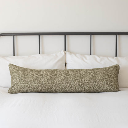 Long rectangular lumbar pillow with green and cream damask pattern on white bedding with black metal headboard.