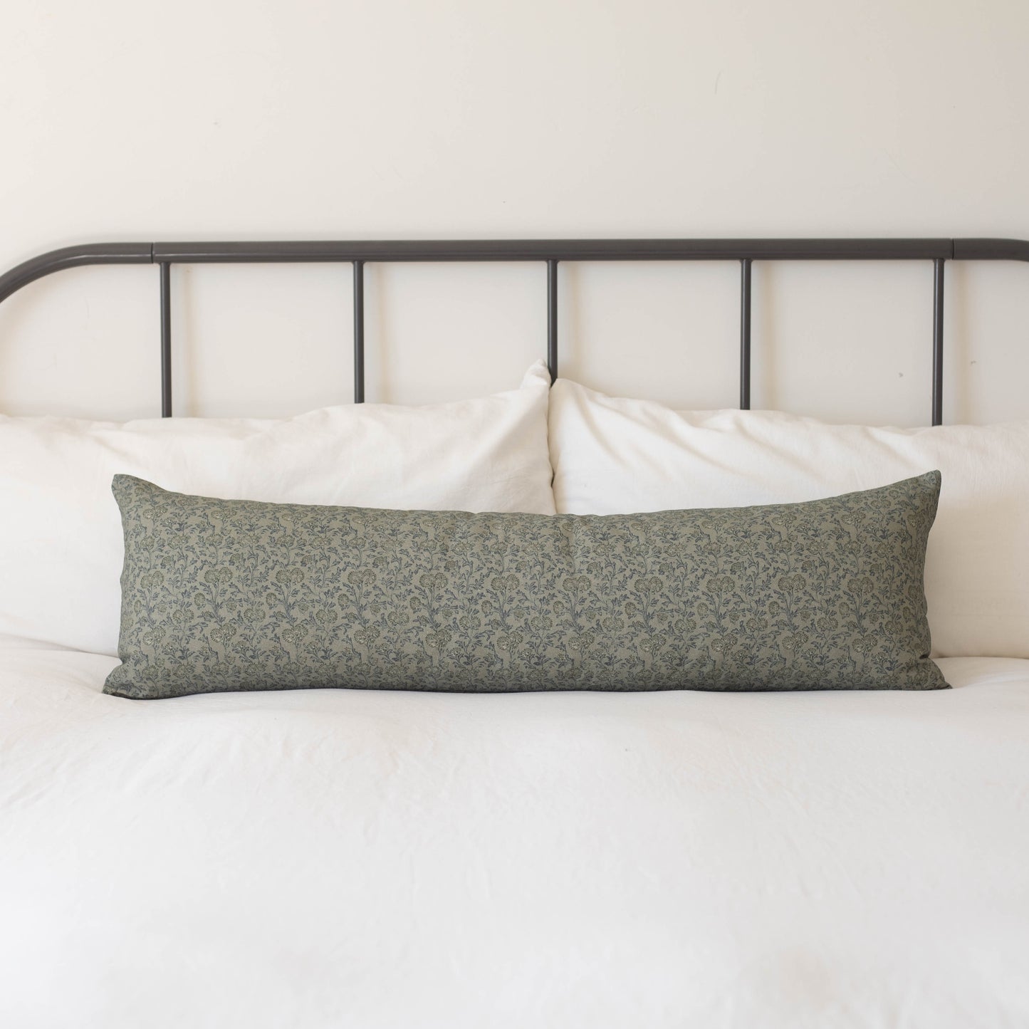 Green floral patterned lumbar pillow on a bed with white bedding and metal headboard.