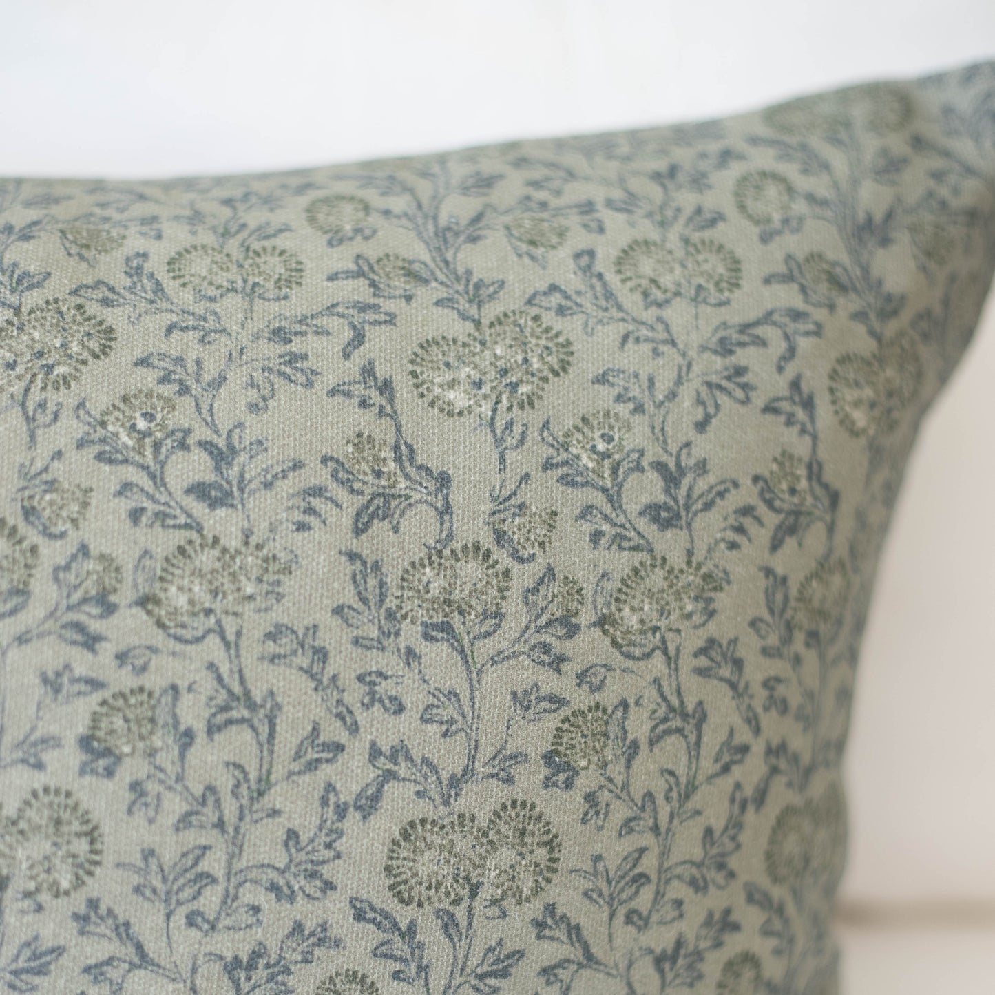 Green pillow with blue and gray botanical floral pattern on linen-textured fabric.