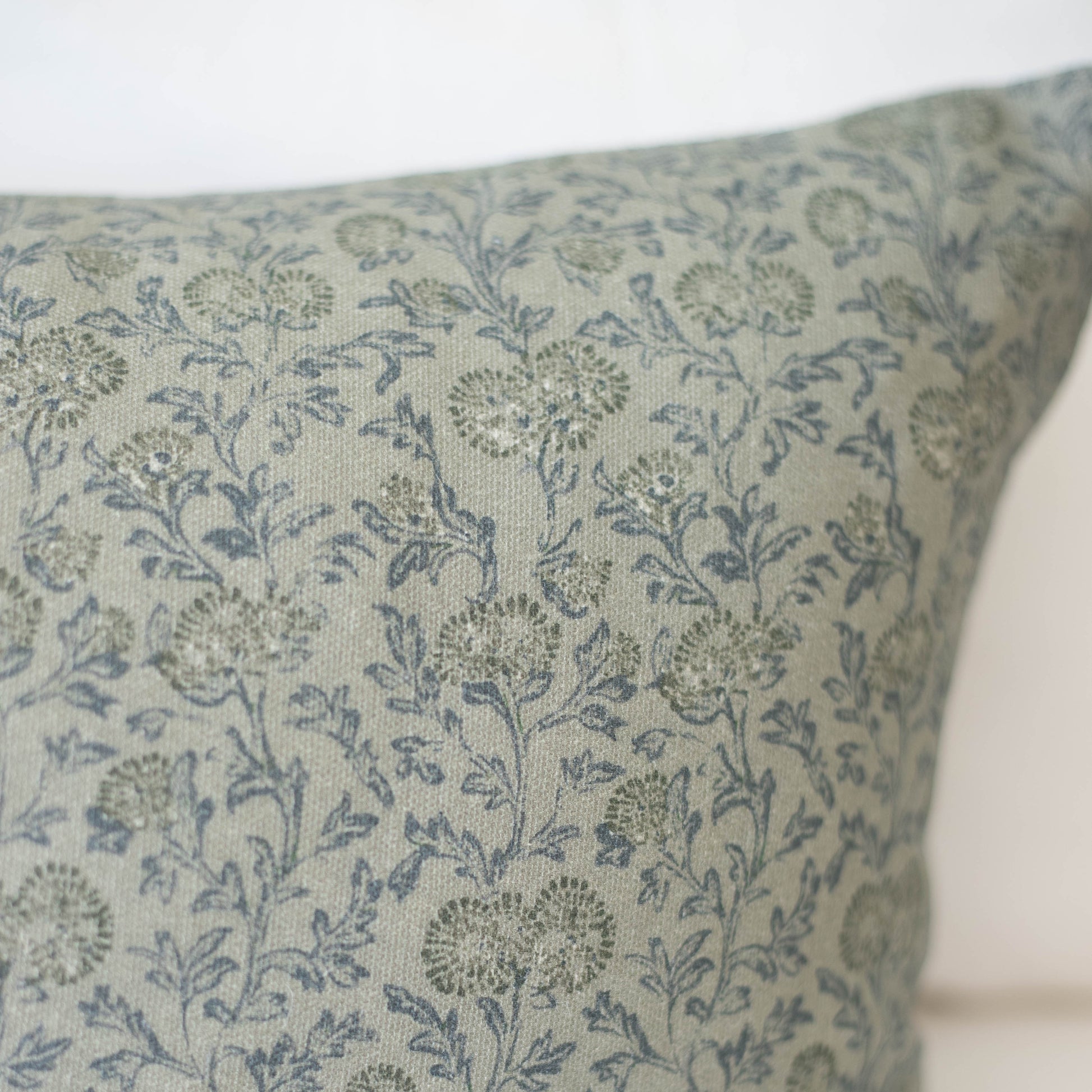 Green pillow with blue and gray botanical floral pattern on linen-textured fabric.