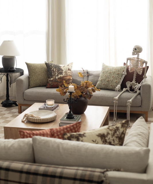Linen throw pillow with autumn harvest scene featuring bare tree and falling leaves in brown and gold tones.
