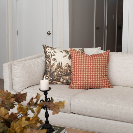 Orange and white gingham plaid square pillow displayed on a cream sofa with coordinating pillows.