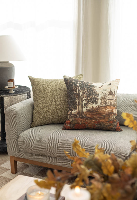 Linen throw pillow with haunted house and gnarled tree design in cream, brown, and rust tones.