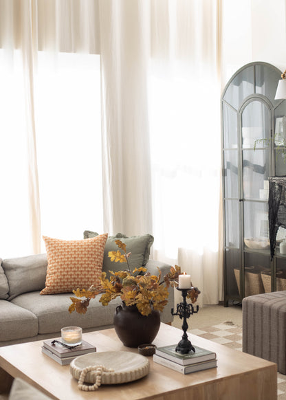 Orange and white gingham patterned pillow displayed on a gray sofa in a living room setting.