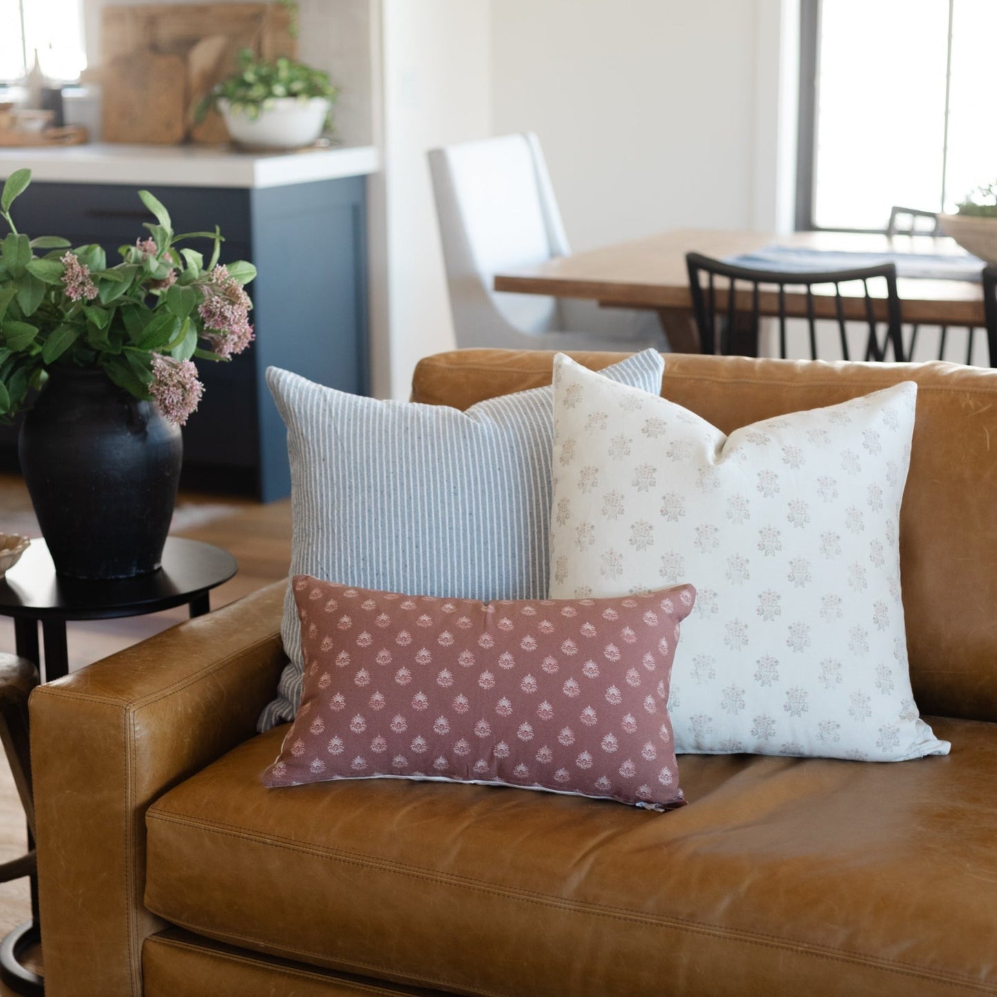 Tan leather sofa with three decorative pillows in striped, floral, and patterned fabrics.