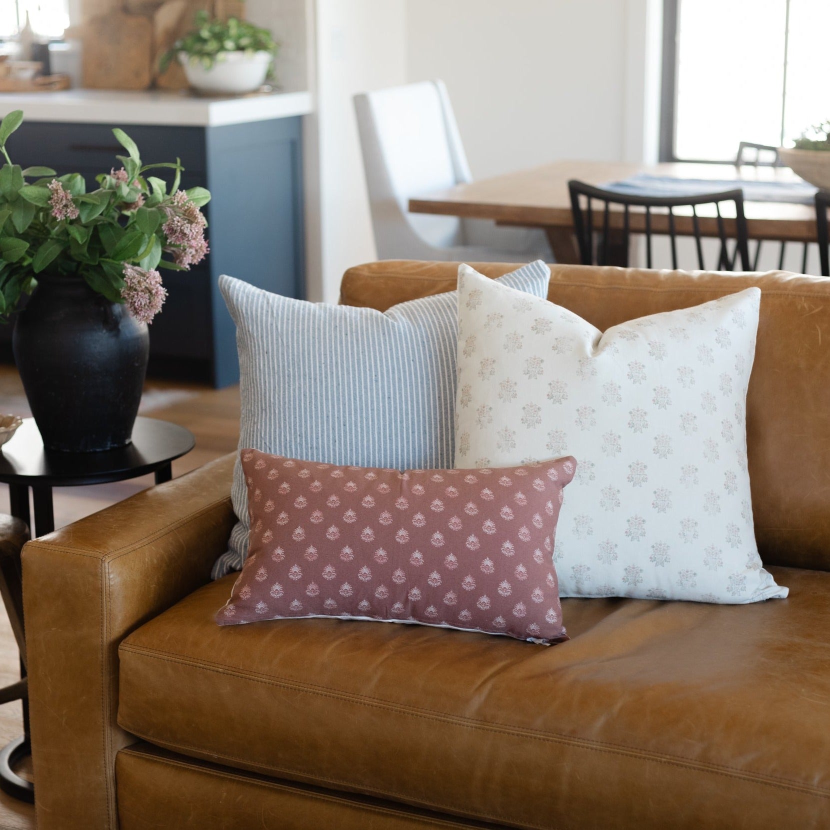 Decorative pillow with small-scale floral print in mauve and cream on tan leather sofa.