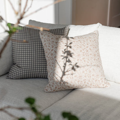 Decorative pillows in gingham check and floral patterns arranged on a gray upholstered sofa with plant shadow overlay.