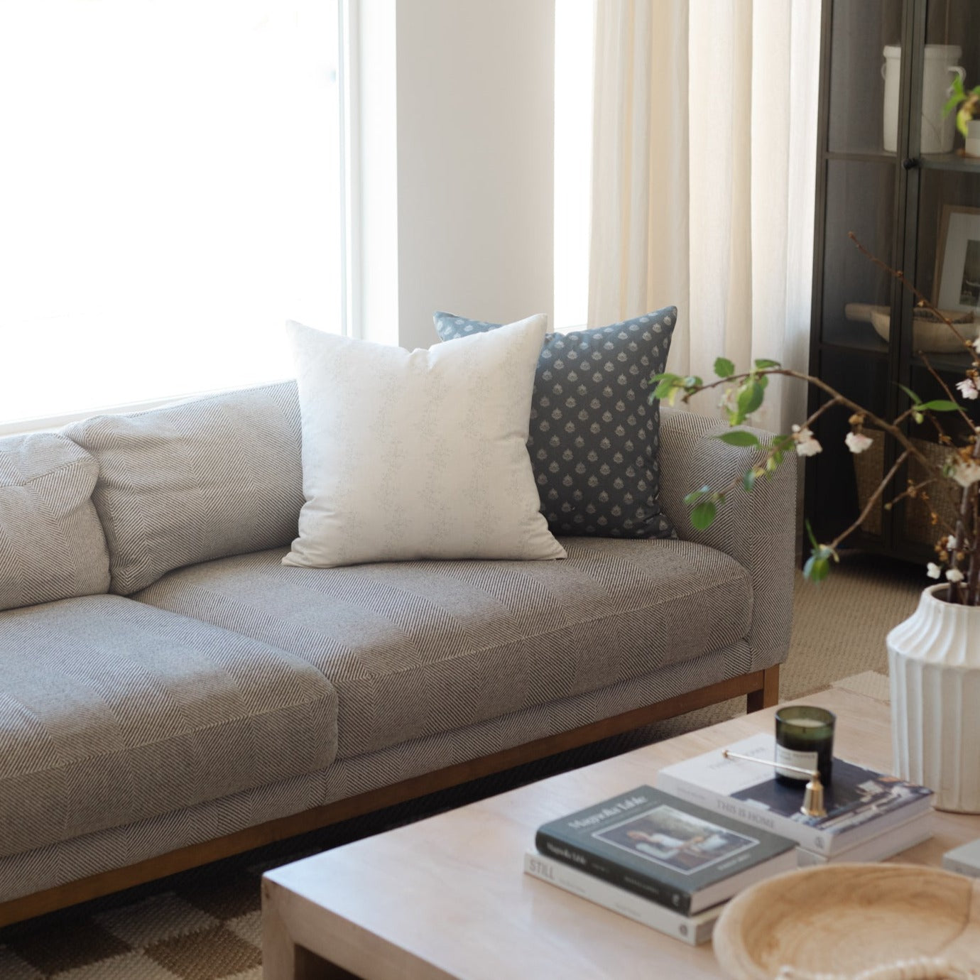 Three decorative pillows on a beige sofa: cream, light blue, and charcoal with dotted pattern.