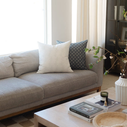 Three decorative pillows on a beige sofa: cream, light blue, and charcoal with dotted pattern.