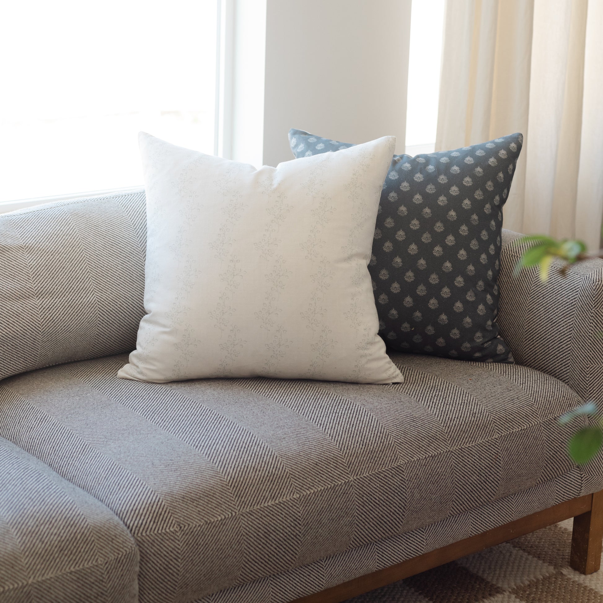 Cream-colored square throw pillow with subtle texture displayed on a patterned sofa with matching pillows.