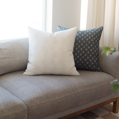 Cream-colored square throw pillow with subtle texture displayed on a patterned sofa with matching pillows.