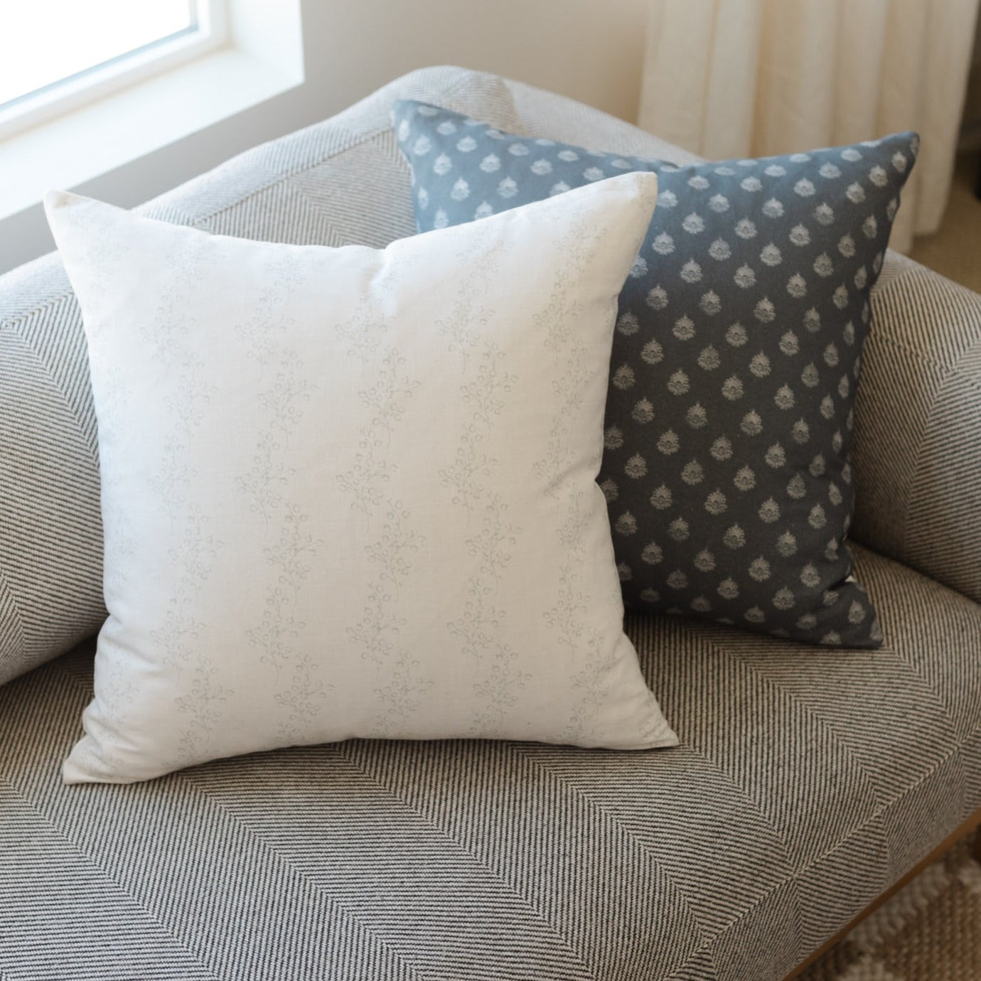White textured pillow with subtle speckled pattern displayed on gray herringbone upholstered seating.