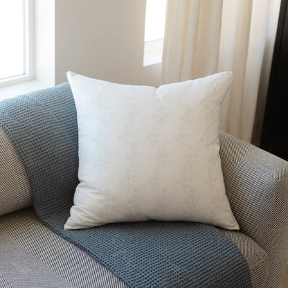 Cream-colored square pillow with subtle dotted texture displayed on a blue patterned sofa.
