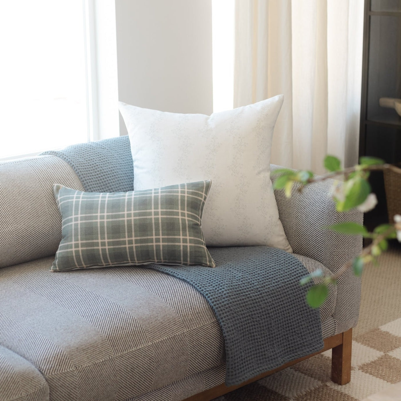 Gray plaid lumbar pillow and cream textured square pillow arranged on a blue upholstered chair.